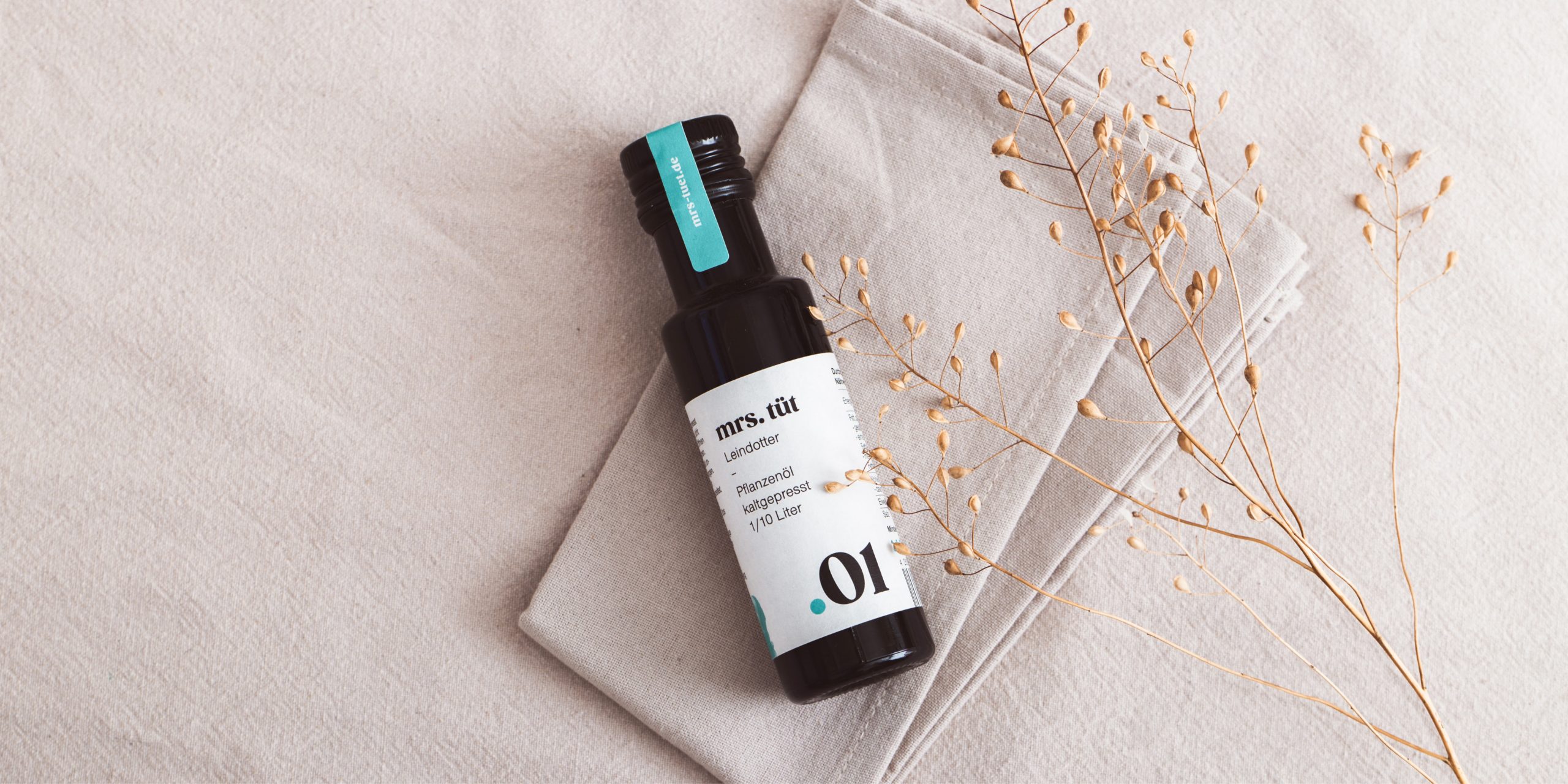 Ölflasche von Mrs. Tüt mit gestaltetem Etikett auf Stoffuntergrund, Beispiel für Produktdesign und Corporate Design
