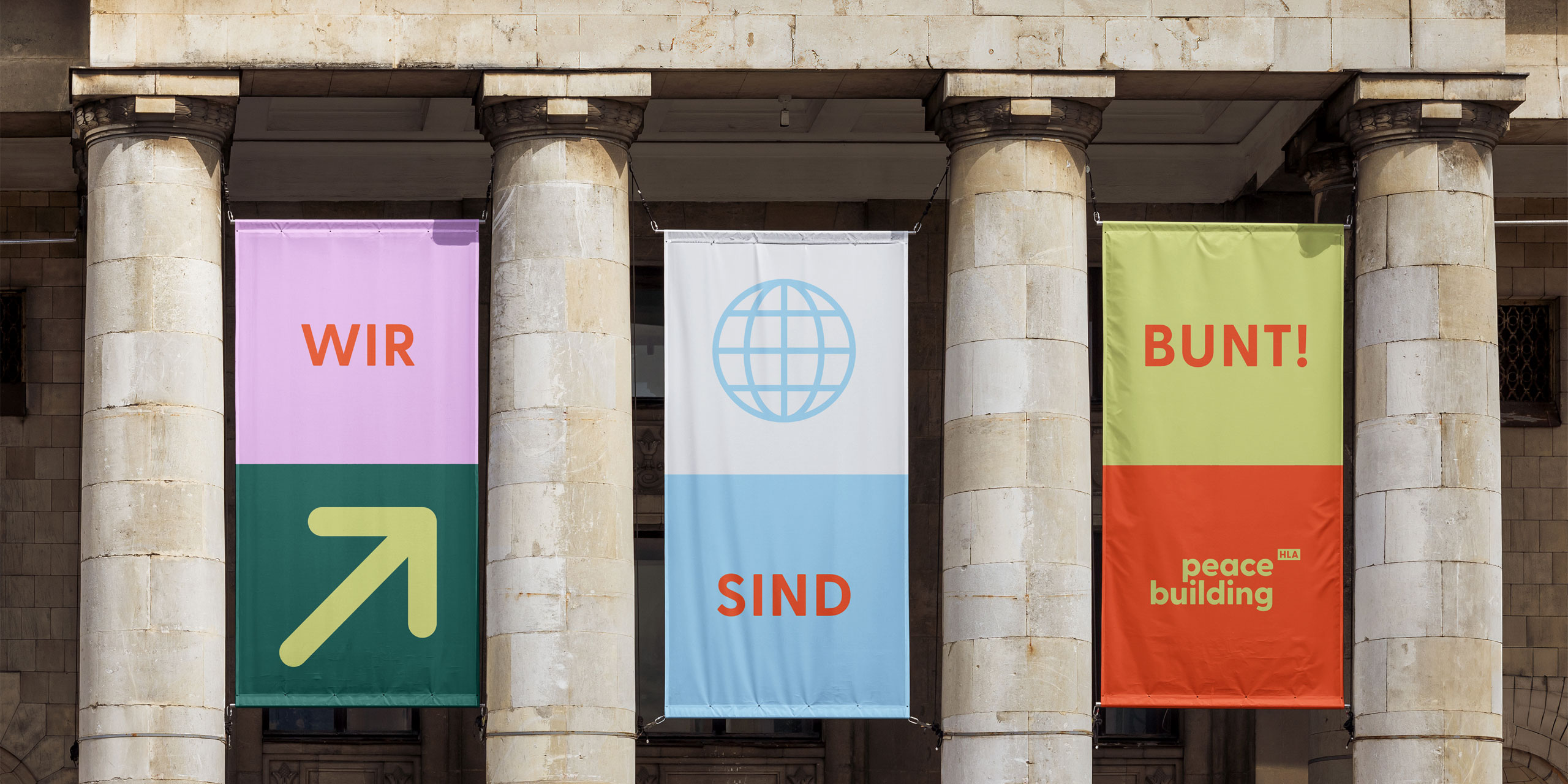 Peace Building – Flaggen mit der Aufschrift ‚Wir sind bunt‘ an den Säulen eines Gebäudes