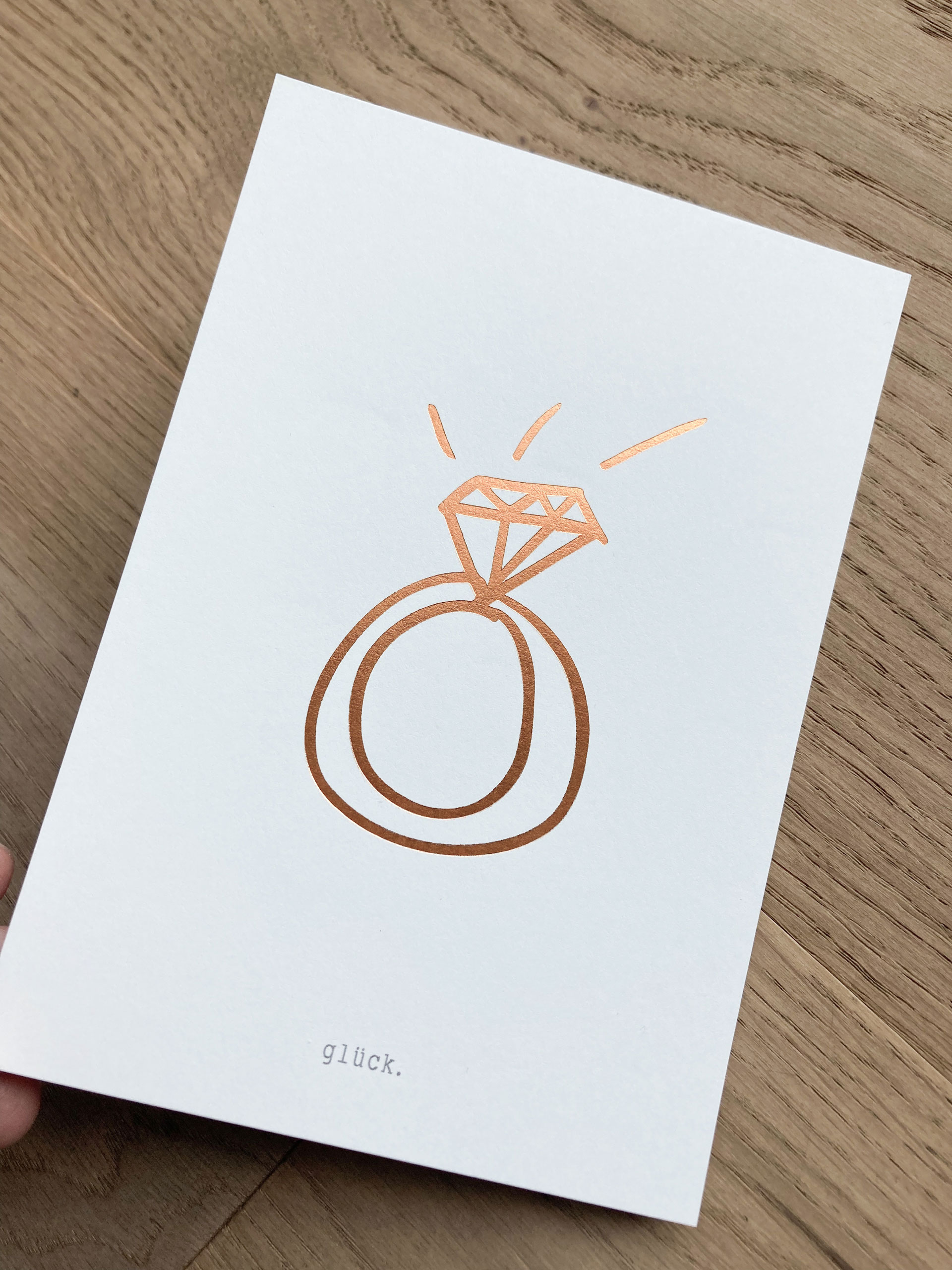 Postkarte der Glücksschmiede Meisterwerkstatt mit illustriertem Ring in Kupferprägung und dem Schriftzug "glück"