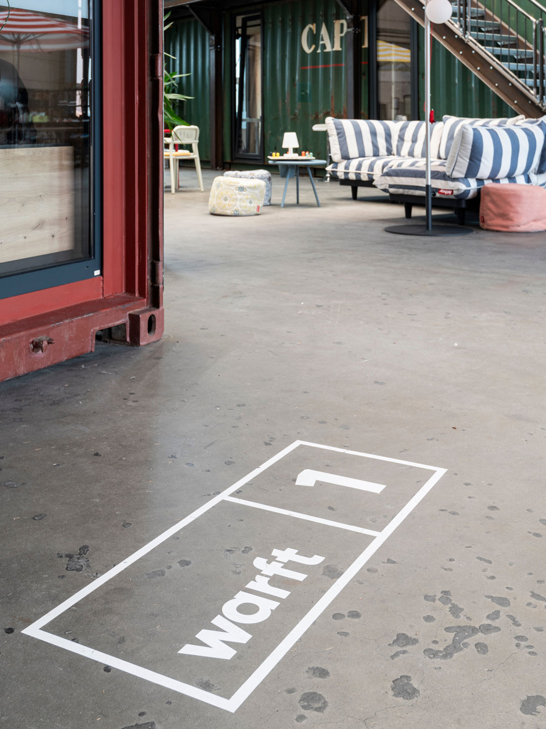 Leitsystem auf dem Boden bei Hallig Hanken: weiße Markierung „warft 1“ mit Sitzgelegenheiten im Hintergrund