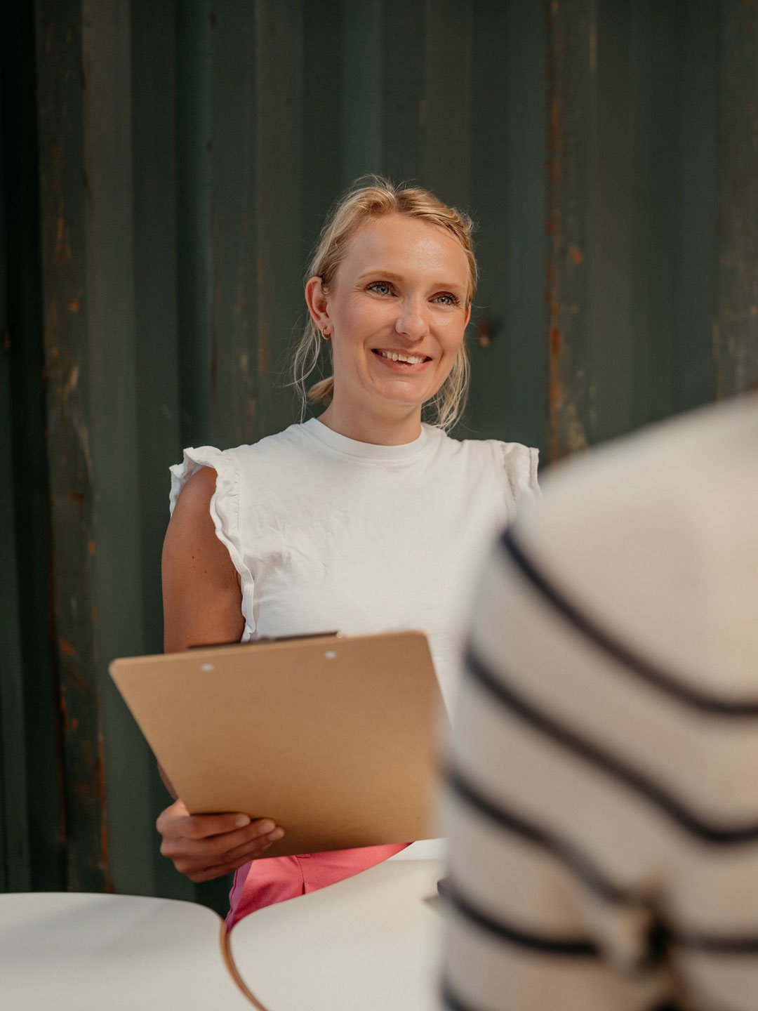 Portrait einer Frau bei Hallig Hanken, freundlich lächelnd mit Klemmbrett in der Hand, vor einem Container-Hintergrund